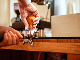 Hand of a barista holding a portafilter and a coffee tamper making an espresso coffee. Barista...