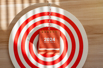 close up 2024 small calendar on dartboard, red dart arrow hitting on target center, planning and...