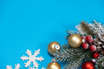 Snow-covered christmas tree branch with red and golden balls on blue background.