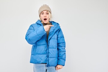 Young woman in blue winter jacket pointing aside finger, demonstrating empty space for product or...