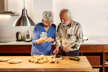 Senior multiracial couple learn new recipes together with their smartphone in the kitchen