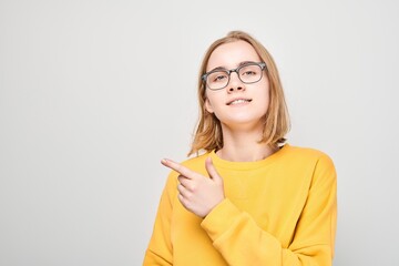 Young blond girl in yellow casual pointing finger aside, demonstrating empty space for product or text isolated on white studio background.