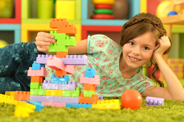 Portrait of cute girl playing with colorful plastic blocks in room