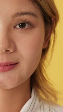 Close-up, half face of woman opening eyes and looking at camera isolated on yellow background