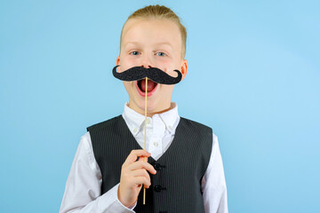 A child in an elegant suit holding mustache on a stick on the blue background. Purim celebration...