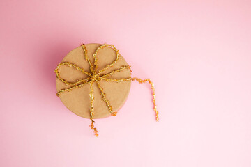 A gift box with a golden ribbon on a pink background. Christmas gift, greeting background. Copy space, flat lay