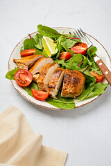 Salad with chicken breast, fillet with lettuce and cherry tomatoes on a plate on a light background..