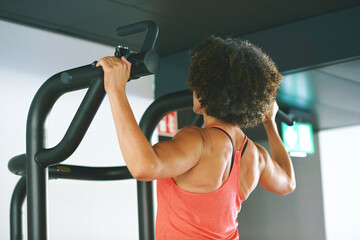 Mature woman exercising on machine at gym for arm and shoulders muscles, back view