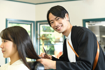 女性客の髪を切るアジア人の男性美容師