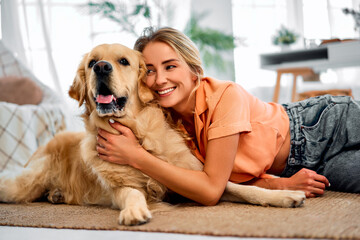 My best friend.Smiling young woman engaging in heartfelt cuddle with her furry companion at living room. Attractive woman sitting on floor and leaning head to head of lovely golden retriever.