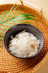 Dried coconut chips in a bowl on a light background vertical photo