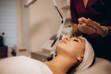 Obraz na płótnie Canvas Cosmetologist applying mask on woman's face in spa salon, closeup