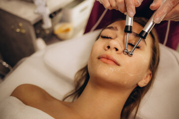 Woman getting microcurrent procedure facelift. Beautician doing anti-aging, to perform facial tightening and toning.