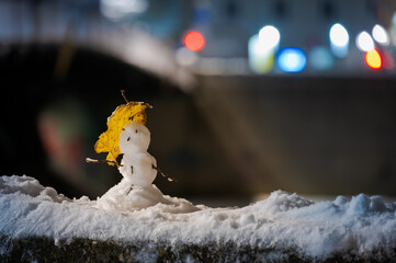 Small cute snow man with umbrella standing on ledge of bridge at night