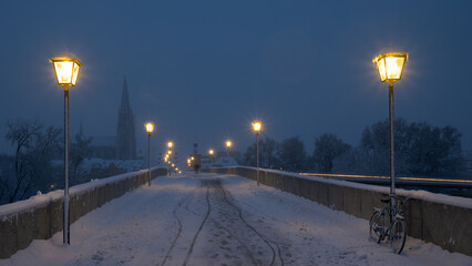 Standing on empty the stone bridge in Regensburg looking south to the cathedral at night in winter with snow