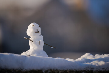 Small cute snow man with umbrella standing on ledge of bridge with urban background out of focus