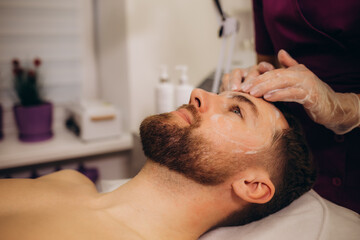 Obraz na płótnie Canvas Beautician applying cosmetic mask on man's face in spa salon