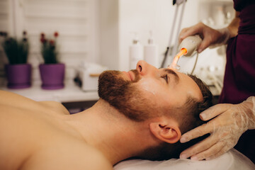 Obraz na płótnie Canvas Darsonval face therapy. Young man, beauty clinic. Ways to improve skin elasticity.