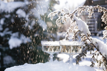 Two crystal glasses of sparkling wine or champagne cooling in snow on winter natural background...