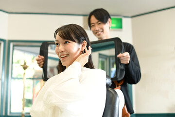 女性客に鏡を見せる美容師のアジア人男性
