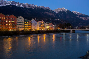 Evening lights reflect on Innsbruck's river with mountains behind