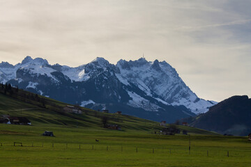 Majestic snow-capped mountains rise over serene green meadows at dusk