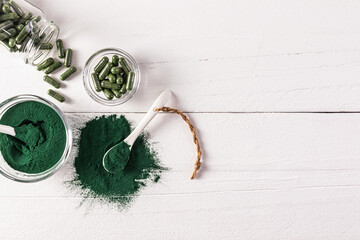 Green spirulina powder, tablets and capsules in various jars on a wooden white table. Top view. A copy space. Biological, natural food additive.