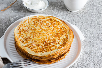 Stack of freshly made pancakes on a ceramic white dish on a grey cement background. A traditional treat for the Spring Festival in Russia.
