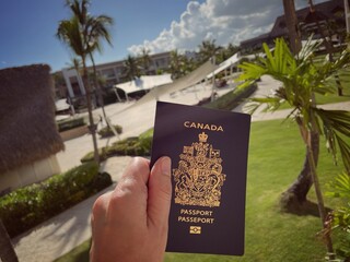 main tenant un passeport canadien sur fond de palmiers et de plantes tropicales dans un complexe hôtelier en République dominicaine - obrazy, fototapety, plakaty
