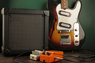 Vintage electric guitar, guitar amplifier and effects pedals for the guitarist against a dark green wall.