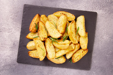 Baked potato wedges with seasonings on a stone tray on a gray st