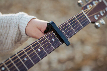 Girl guitarist clinging capo to guitar. Play the guitar using a capo (musical device)