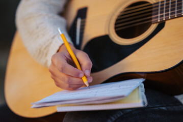 Close up of a girl musician composing song, writing down chords to the notes. Playing the guitar,...