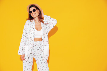 Young beautiful smiling female in trendy summer costume clothes. Carefree woman posing near yellow wall in studio. Positive model having fun indoors. Cheerful and happy. In hat and sunglasses