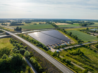 Drone Shot of solar panels at a sunny day between fields, river and a street.
