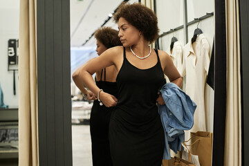 Medium full shot of young african american shop visitor trying on black dress in fitting room