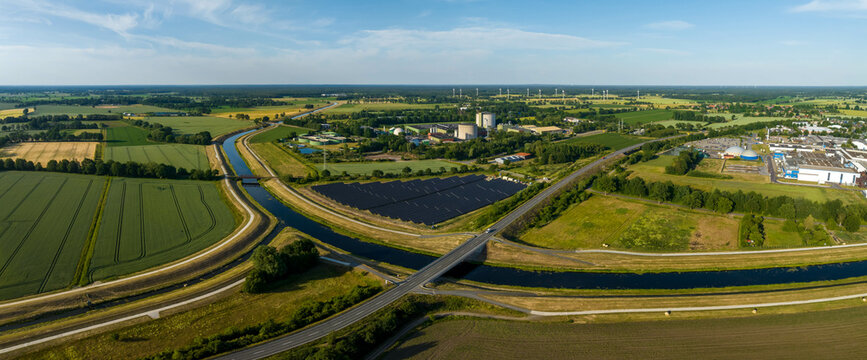 Panorama of solar panels at a sunny day between fields, river and a street.