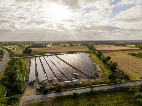 Drone Shot of solar panels at a sunny day between fields, river and a street.