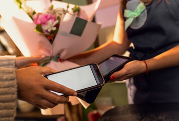 Close up of female hands smart phone for paying using payment terminal in flower shop.
