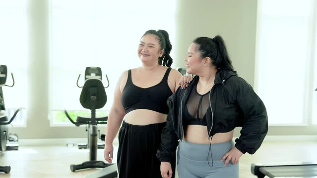 Two chubby Asian women, standing together in fitness center doing weight loss exercises for sedentary health, women are friends often invite each other come, standing taking photo before exercising.