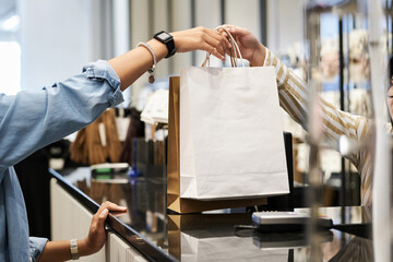 Unrecognizable cashier giving paper bags with purchases to unknown customer at clothing store - obrazy, fototapety, plakaty
