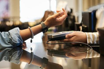 Unrecognizable woman paying with her digital wristwatch at store, unknown cashier receiving payment