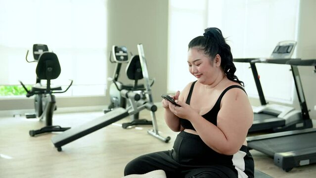Asian woman, overweight body, sits in fitness center, full exercise equipment, come here for slimming exercises, for health, but since wasn't quite ready, sat played with my cell phone for fun.