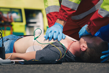 Hands of paramedic and doctor during resuscitation on road against ambulance car. Patient and team...