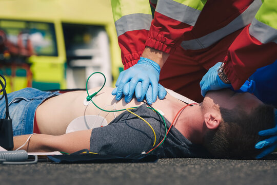 Hands of paramedic and doctor during resuscitation on road against ambulance car. Patient and team of emergency medical service. Themes rescue, urgency and health care..