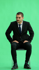young man in full growth. isolated on a green background sitting on a chair