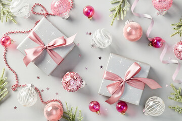 Christmas flat lay composition with gift boxes decorated pink ribbon bows, glitter baubles, fir branches, confetti on grey background.