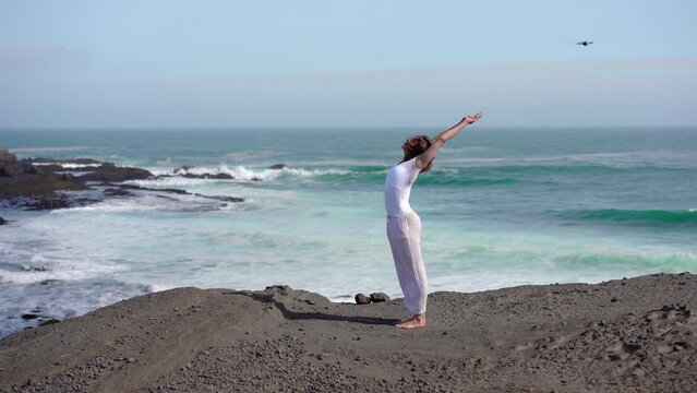 Girl doing yoga on a rock near the ocean, view from a drone in Iceland