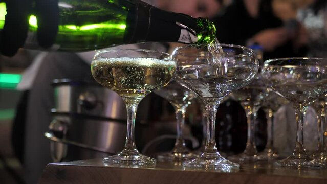the waiter pours champagne into glasses and distributes the filled glasses to the guests. close-up.