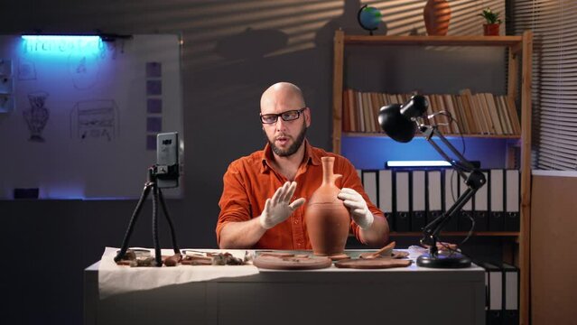 Archaeologist leading a scientific blog talking about an ancient amphora recording a video using a smartphone on a tripod, working overtime